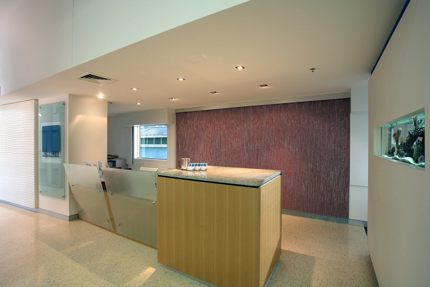 Office lobby with a timber and glass reception desk, inset aquarium, and a feature red wall covered in chains.