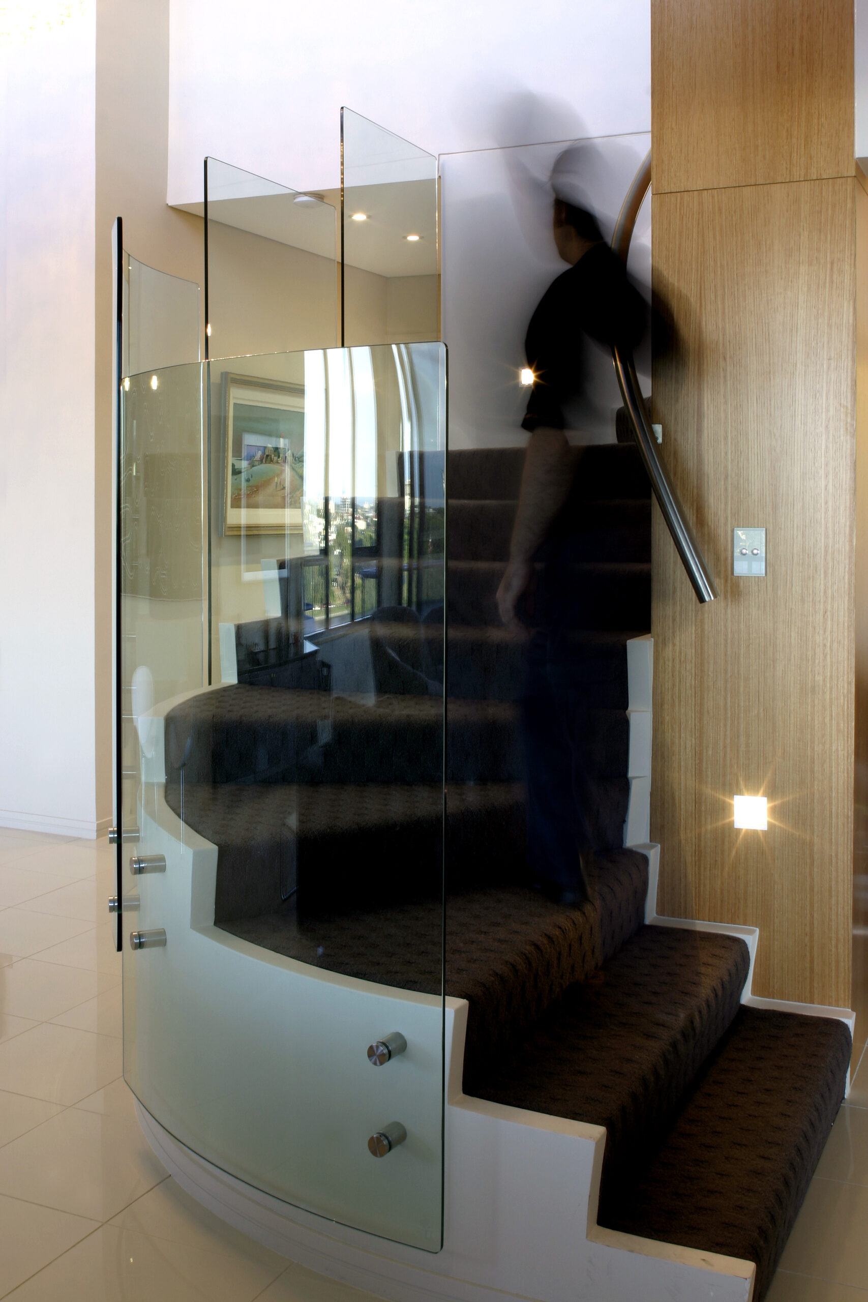 Interior of a penthouse showcasing a spiral staircase with an intricately designed handle running alongside. Adjacent to the stairs, a sparkling crystal chandelier illuminates the space