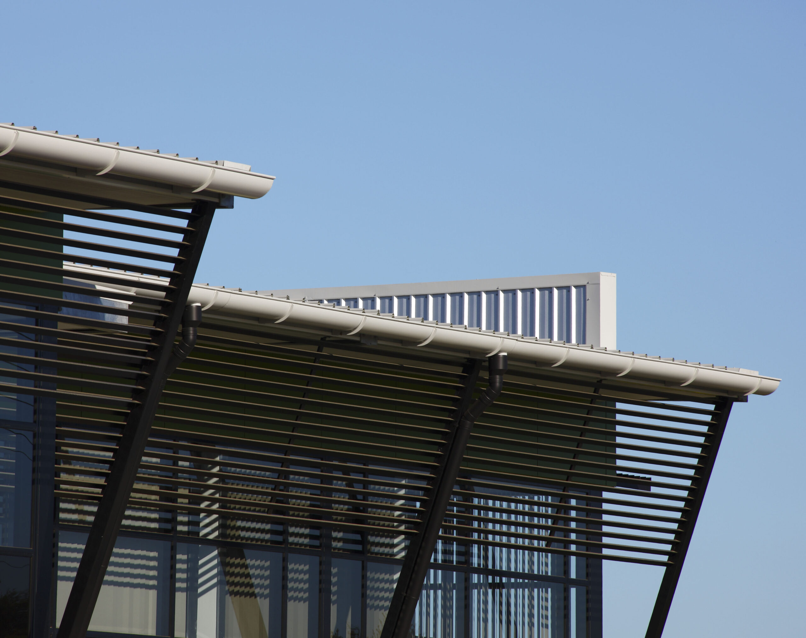 Close-up of the junction between a warehouse roof and angled columns, featuring aluminum horizontal shading elements extending up to the roof's base