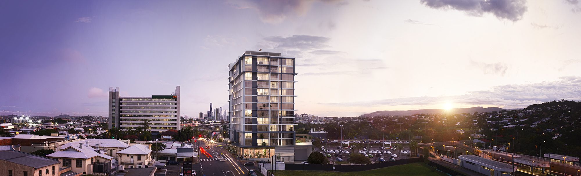 Mid-rise apartment building in Brisbane located adjacent to a train station at sunset, captured from an elevated perspective to showcase its contextual relationships.